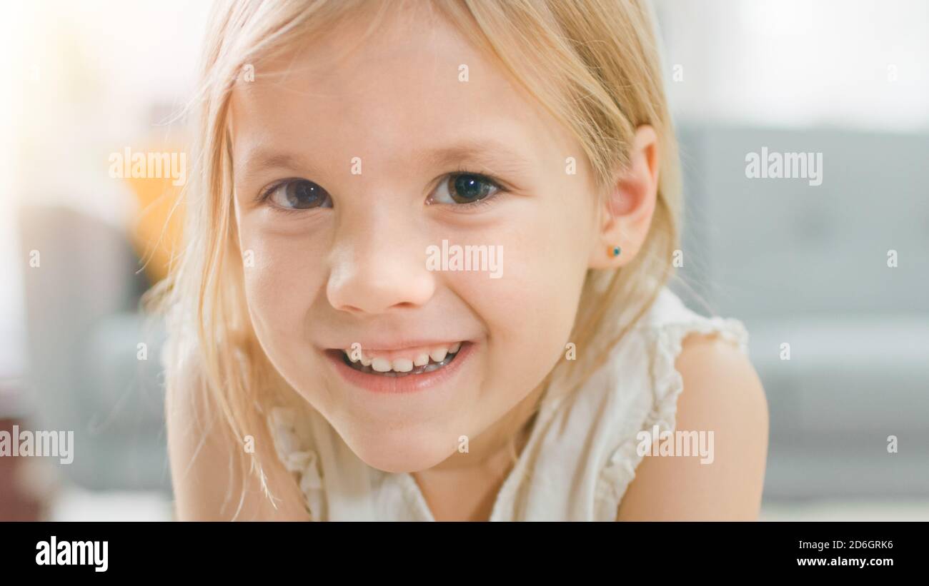 Portrait of Sweet Cute Happy Young Blonde Girl Smiling on Camera. In the Background Blurred Sunny Room. Stock Photo