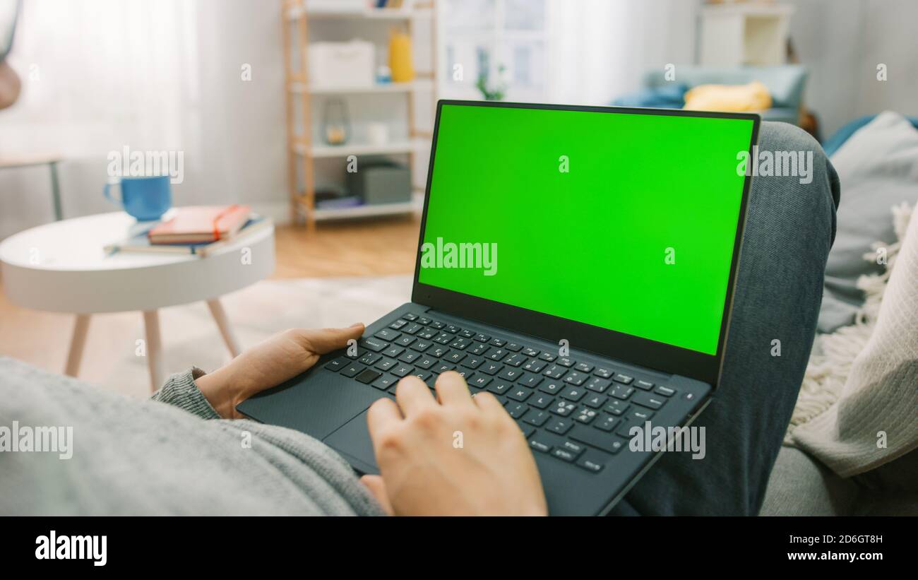Man at Home Laying on a Couch Using with Green Mockup Screen Laptop