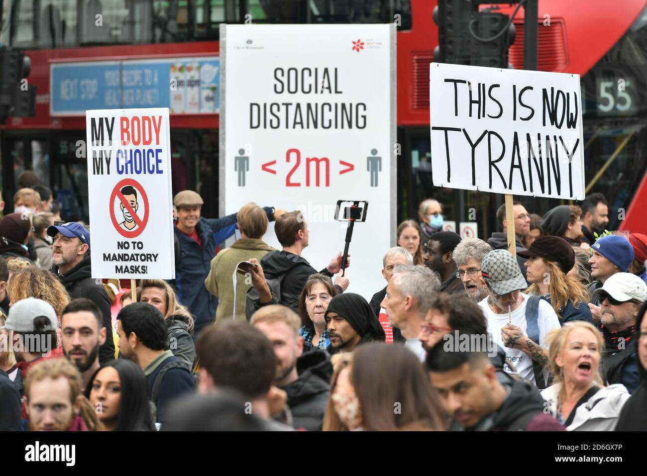 Protesters during an anti-lockdown rally pass a social distancing sign on Tottenham Court Road, London. Stock Photo