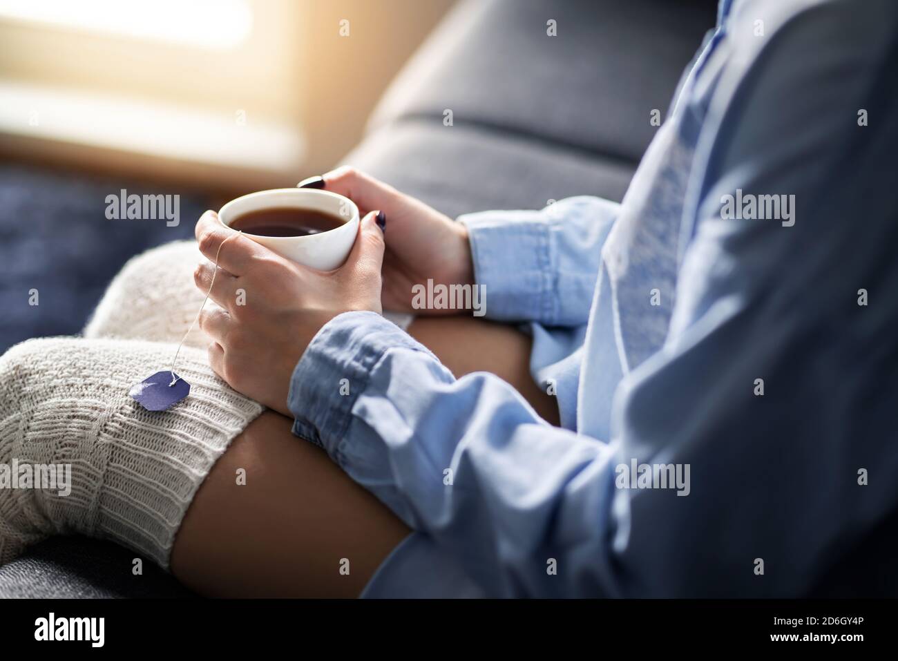Cold winter morning comfort at home with warm tea. Happy woman holding hot cup. Sick person with flu or fever. Relaxing on comfy couch. Stock Photo
