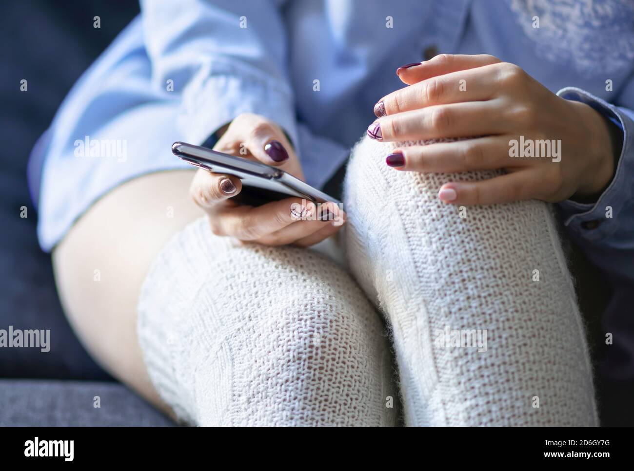 Texting and using phone in winter. Hipster woman with cellphone lying on home couch. Sending sms message with smartphone. Girl online shopping. Stock Photo