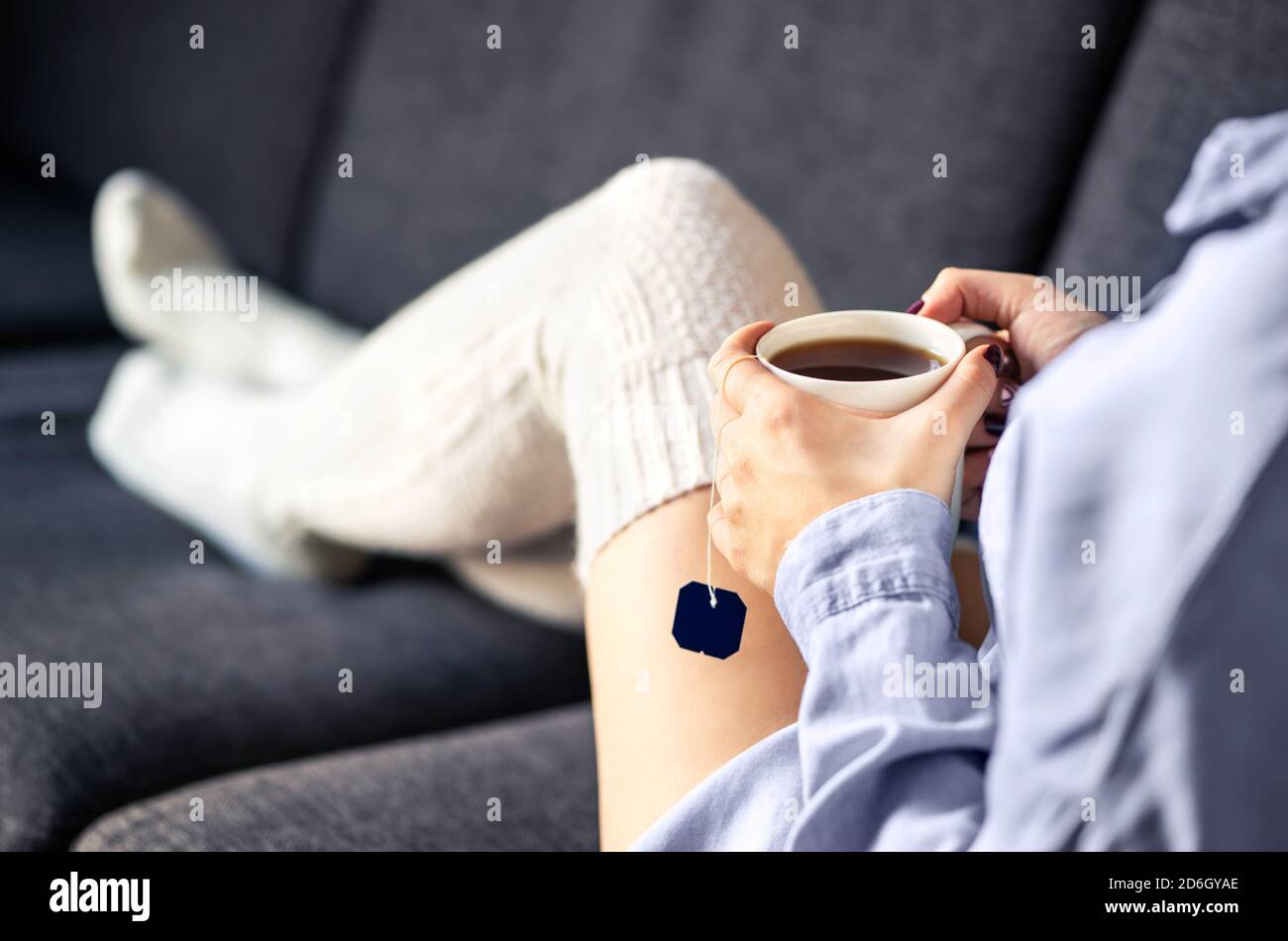 Woman in comfy warm socks drinking cup of tea in winter. Home comfort and relaxed morning on weekend. Trendy fashion style for the season. Stock Photo