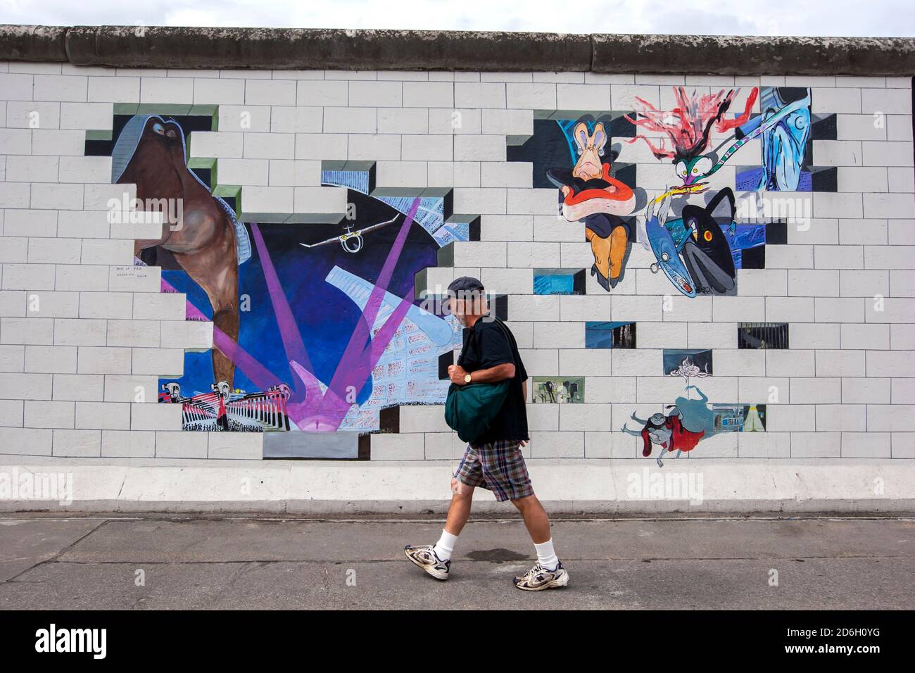 A man walks past a colourful mural covering a section of the former  Berlin Wall in Germany. The Berlin Wall was a barrier that divided the city. Stock Photo