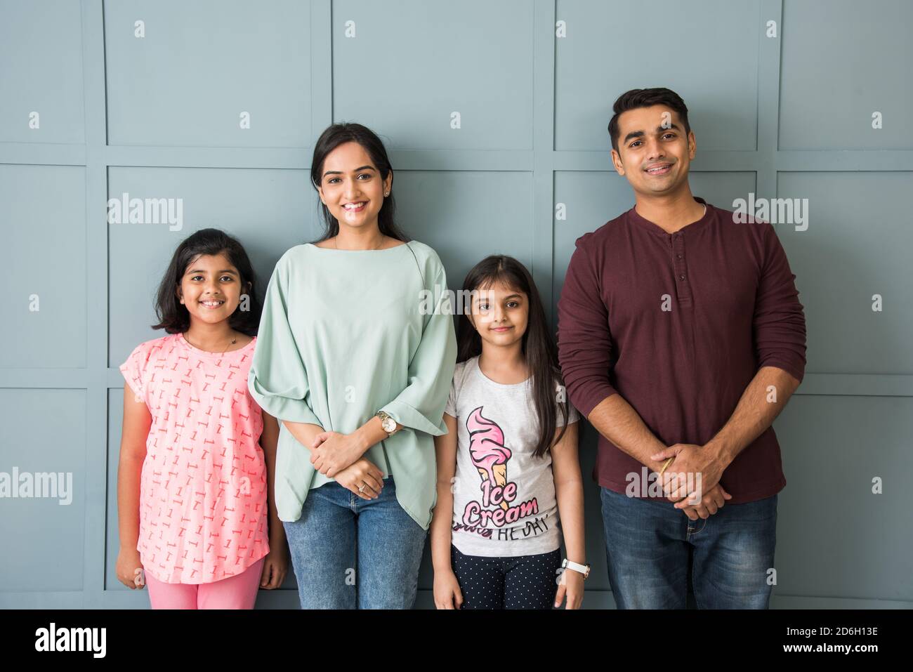 Portrait of happy Indian Asian young family while standing against wall ...