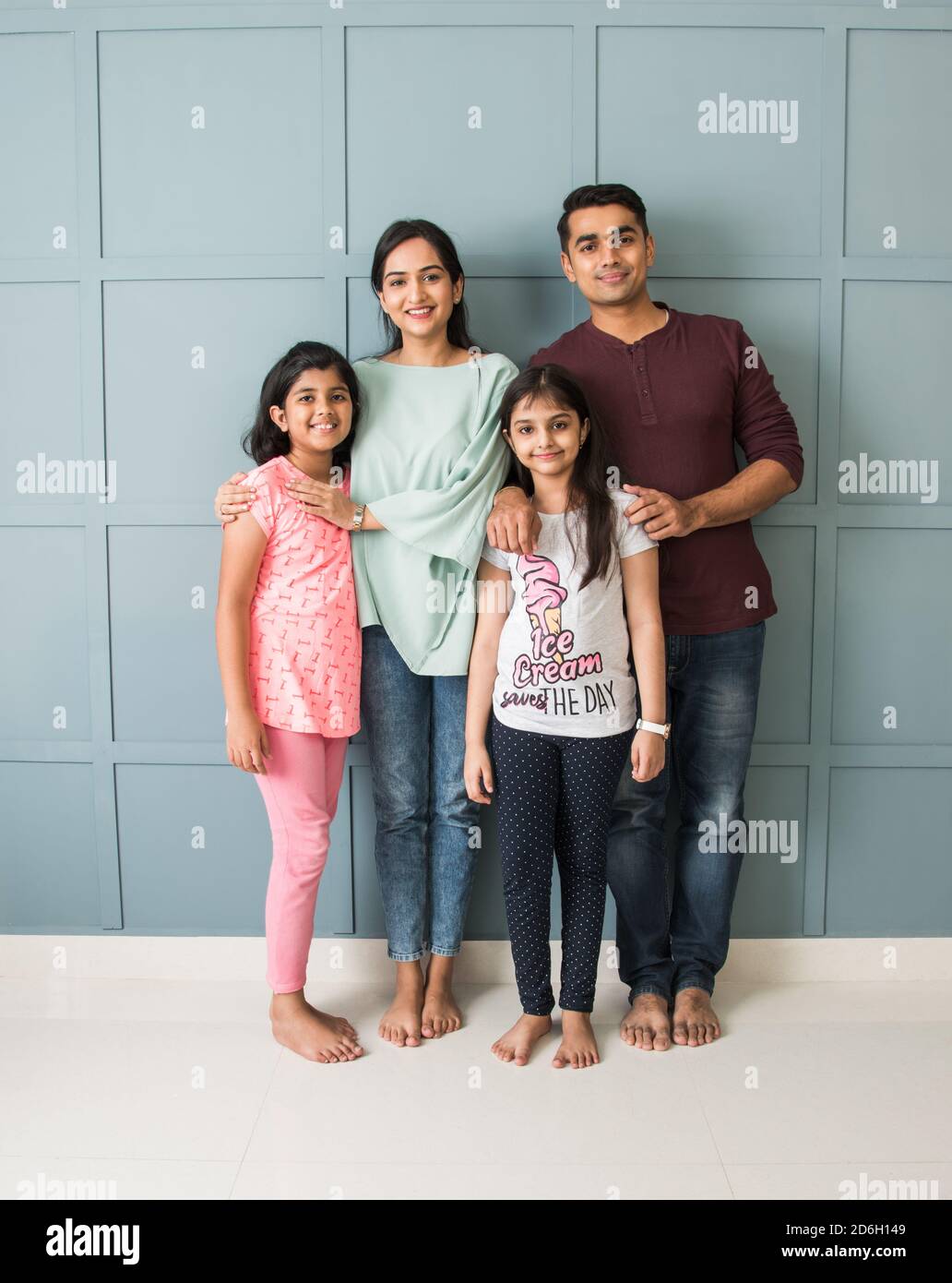 Portrait of happy Indian Asian young family while standing against wall, parents with two daughters looking at camera Stock Photo