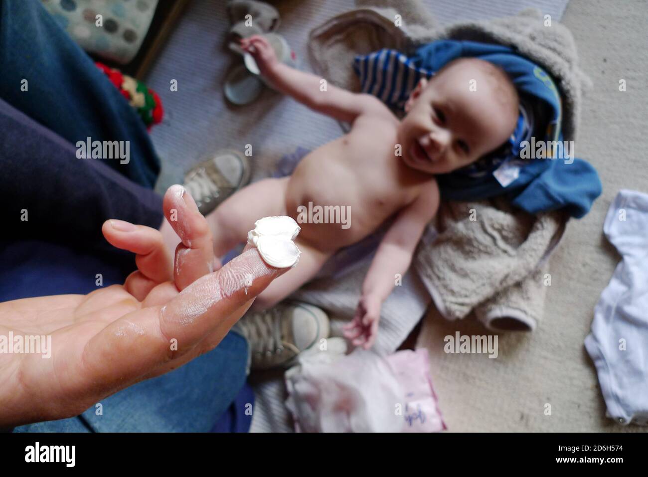 Father Dad changing nappy diaper holding finger of Sudocrem above a happy smiling baby lying on the floor amidst clothing in Wales UK  KATHY DEWITT Stock Photo