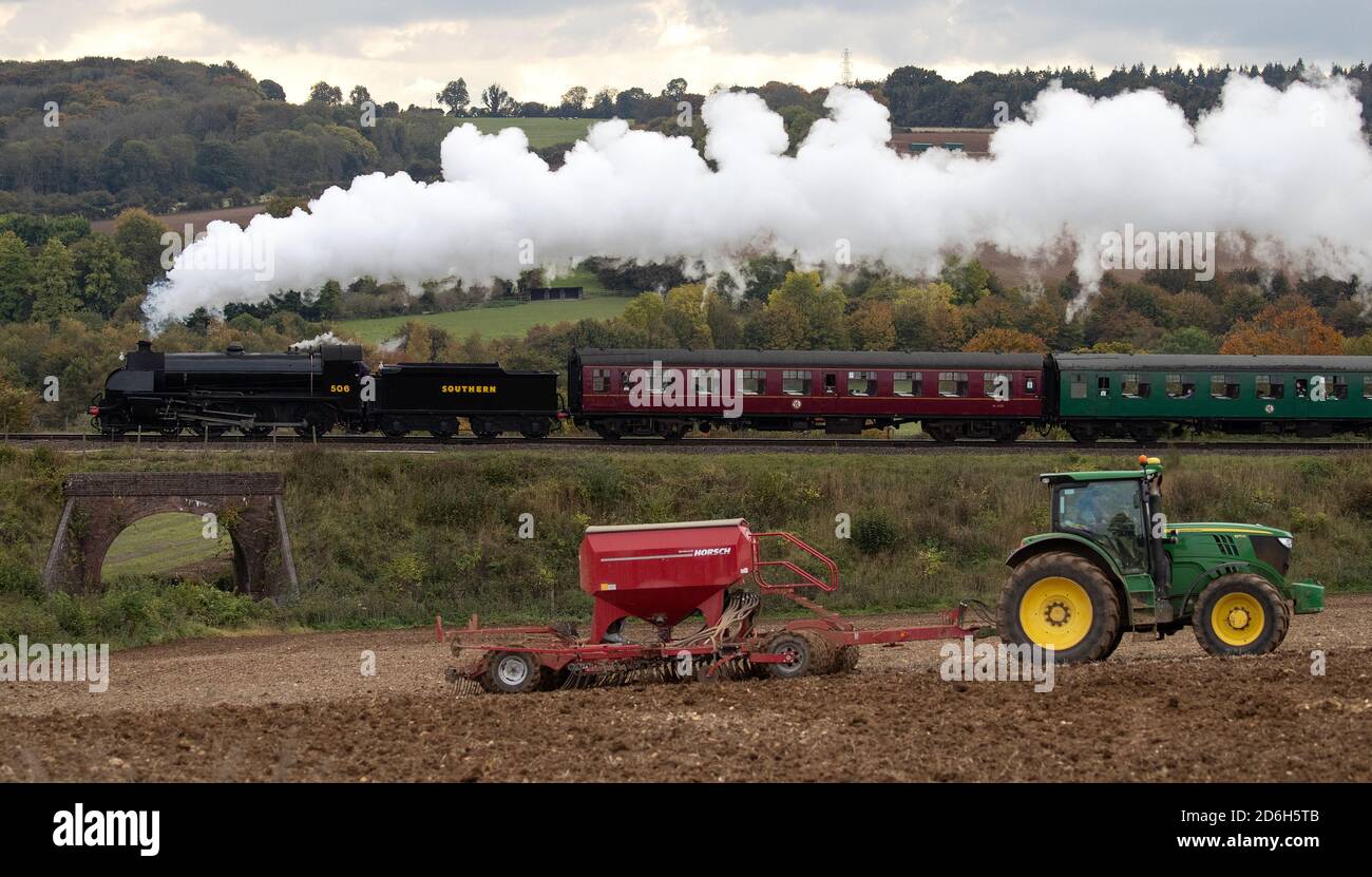 The S15 class steam locomotive 506 passes a tractor in a field as it makes it's along the Mid Hants Railway, also known as the Watercress line, near to Ropley in Hampshire during the weekend's Autumn Steam Gala. Stock Photo