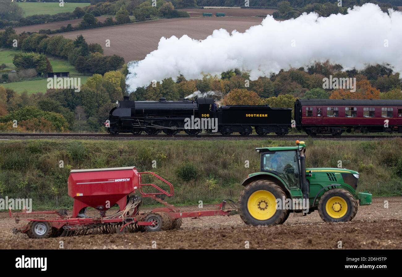 The S15 class steam locomotive 506 passes a tractor in a field as it makes it's along the Mid Hants Railway, also known as the Watercress line, near to Ropley in Hampshire during the weekend's Autumn Steam Gala. Stock Photo