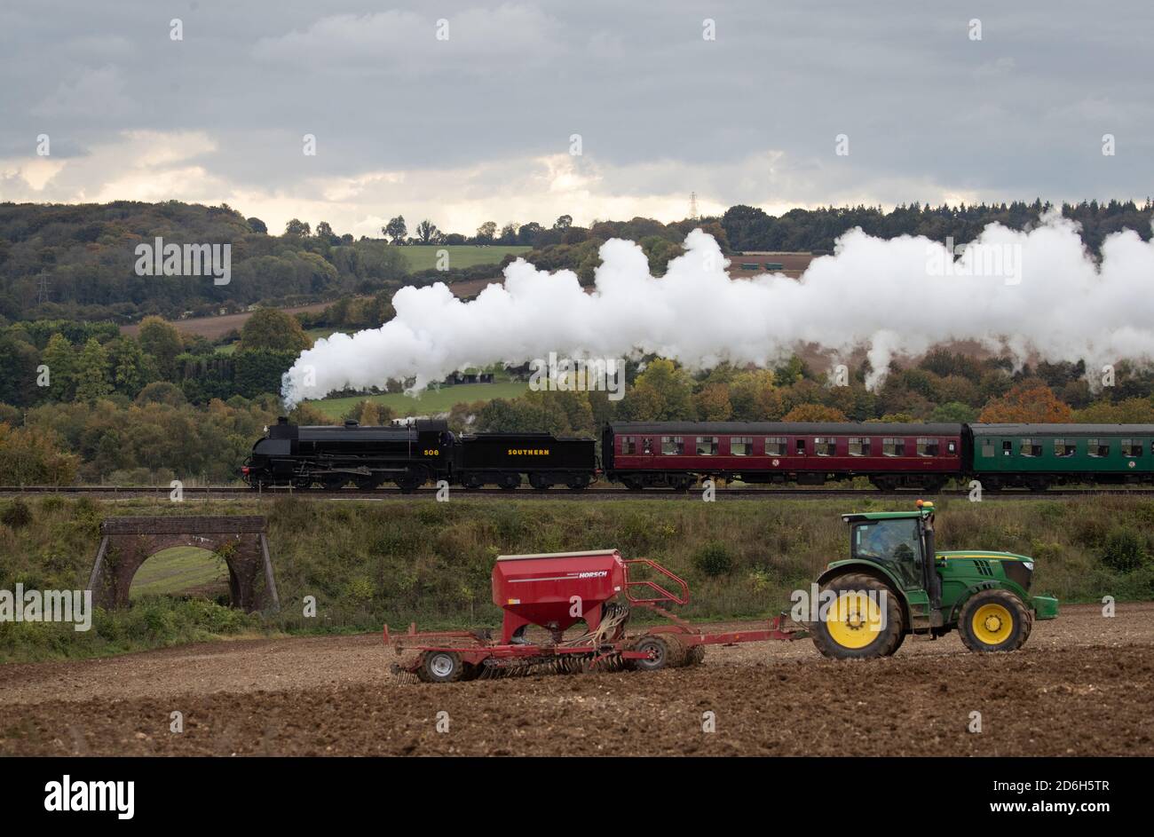 The S15 class steam locomotive 506 passes a tractor in a field as it makes it's along the Mid Hants Railway, also known as the Watercress line, near to Ropley in Hampshire during the weekend's Autumn Steam Gala. Stock Photo