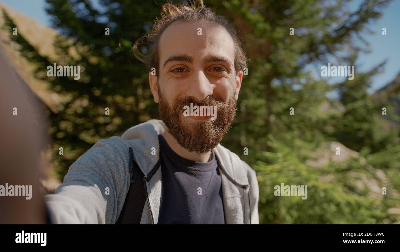 Hippie climber with his backpack behind him, with his handheld camera or phone, salutes the audience or the person he is talking, vlogger or video cha Stock Photo
