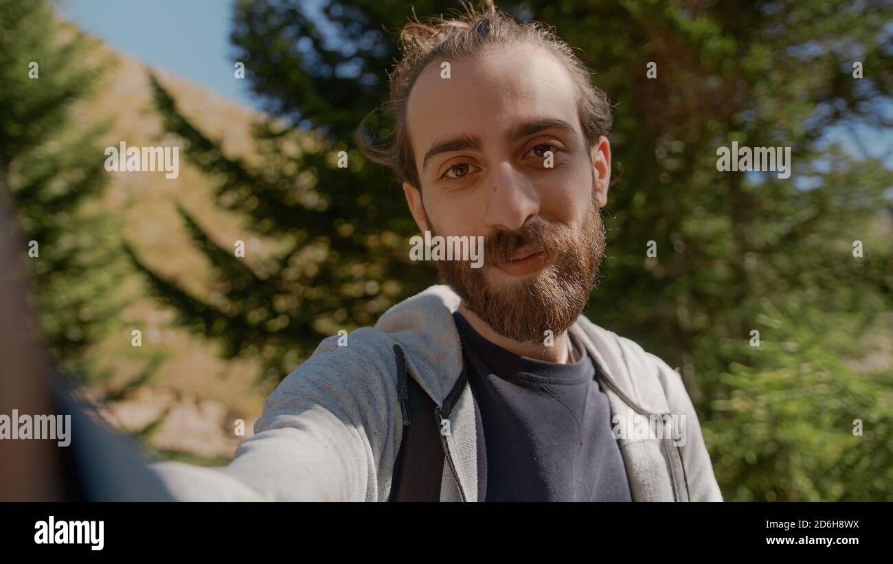 Hippie climber with his backpack behind him, with his handheld camera or phone, salutes the audience or the person he is talking, vlogger or video cha Stock Photo