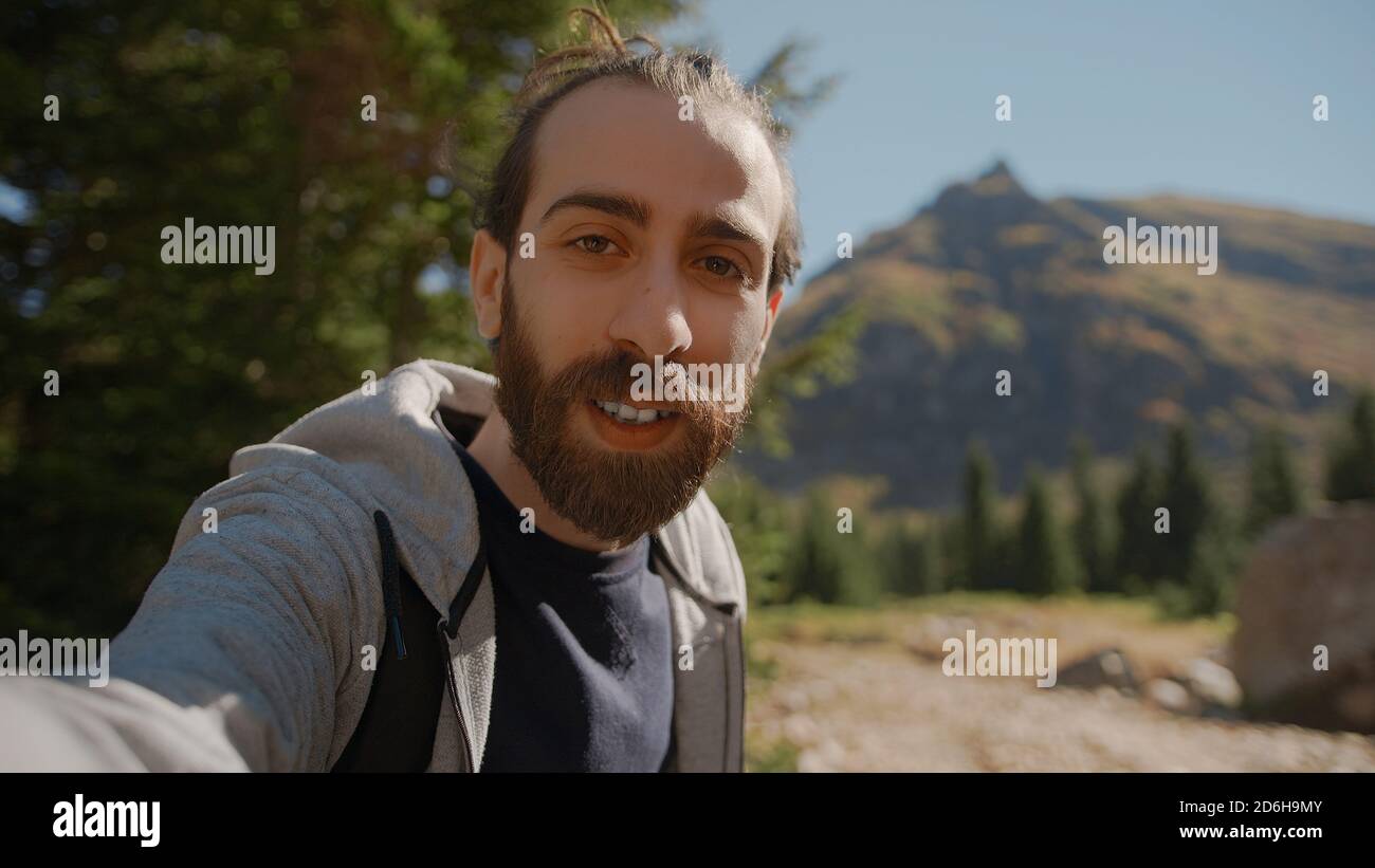 Hippie climber with his backpack behind him, with his handheld camera or phone, salutes the audience or the person he is talking, vlogger or video cha Stock Photo