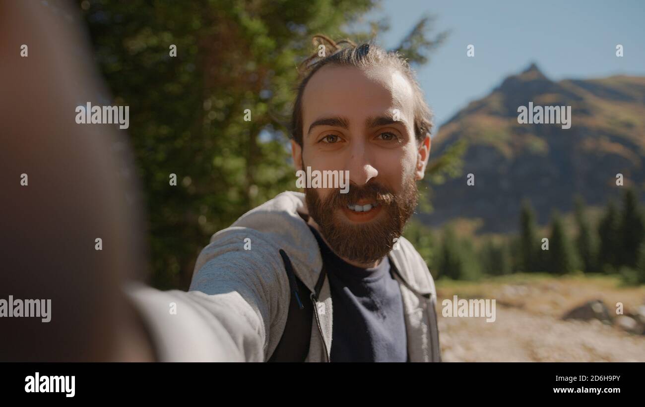 Hippie climber with his backpack behind him, with his handheld camera or phone, salutes the audience or the person he is talking, vlogger or video cha Stock Photo