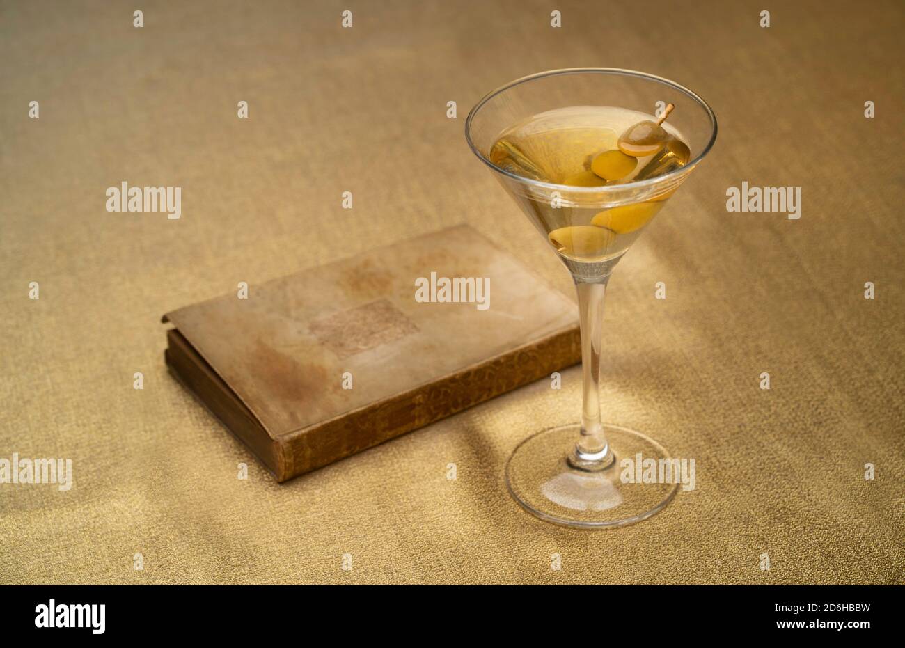 vodka martini cocktail with olives and an old brown book on golden cloth Stock Photo