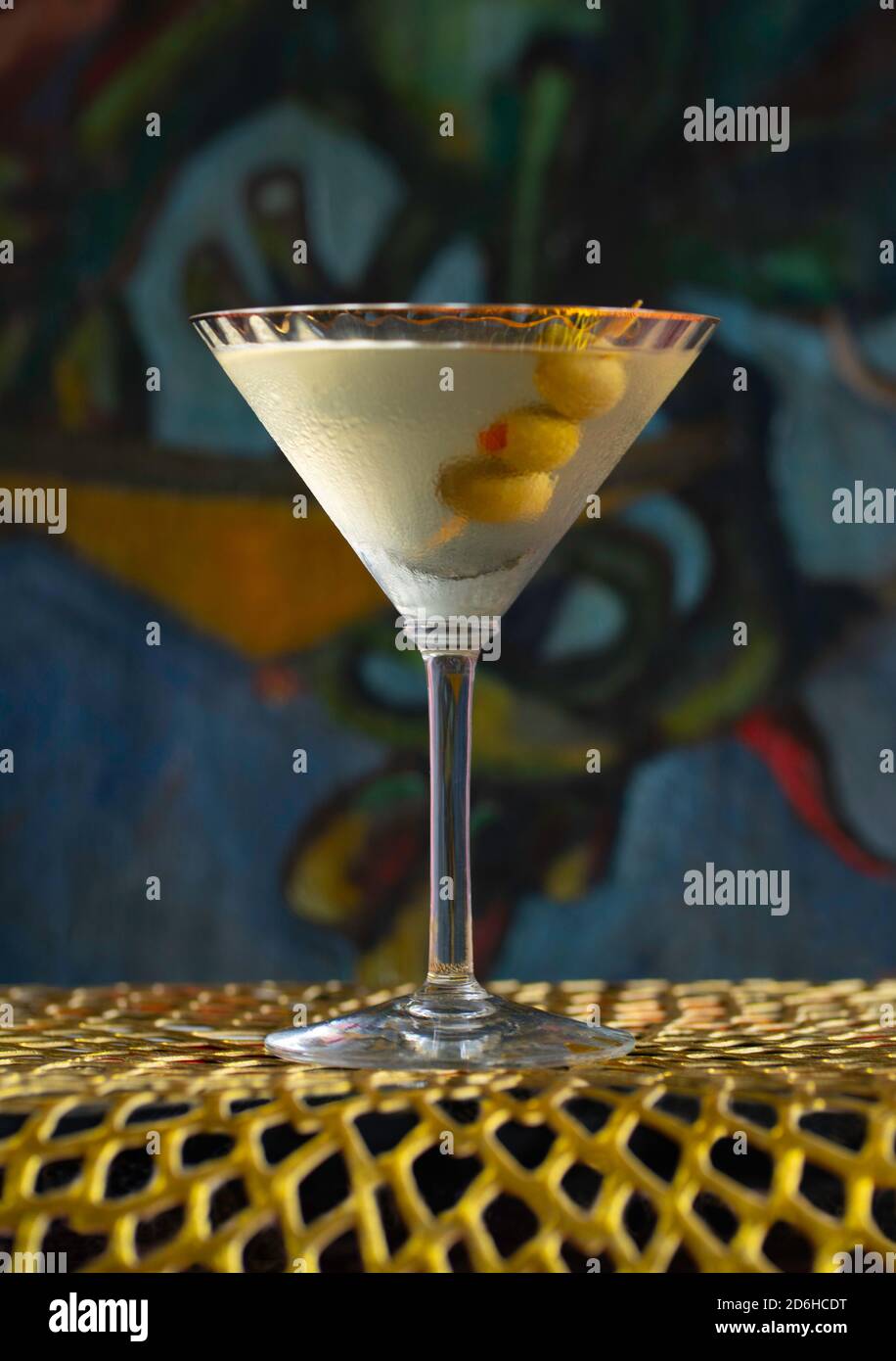 Vodka martini cocktail drink with olives on gold mat in front of painting Stock Photo