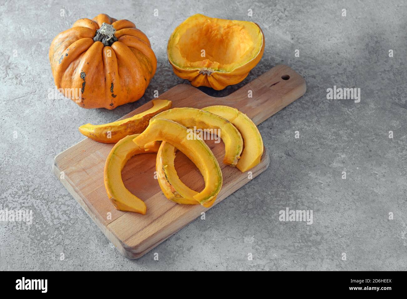 Kamo-Kamo pumpkin or squashwhole and cut in slices on a kitchen board and a gray concrete background, cooking seasonal vegetable for a delicious autum Stock Photo