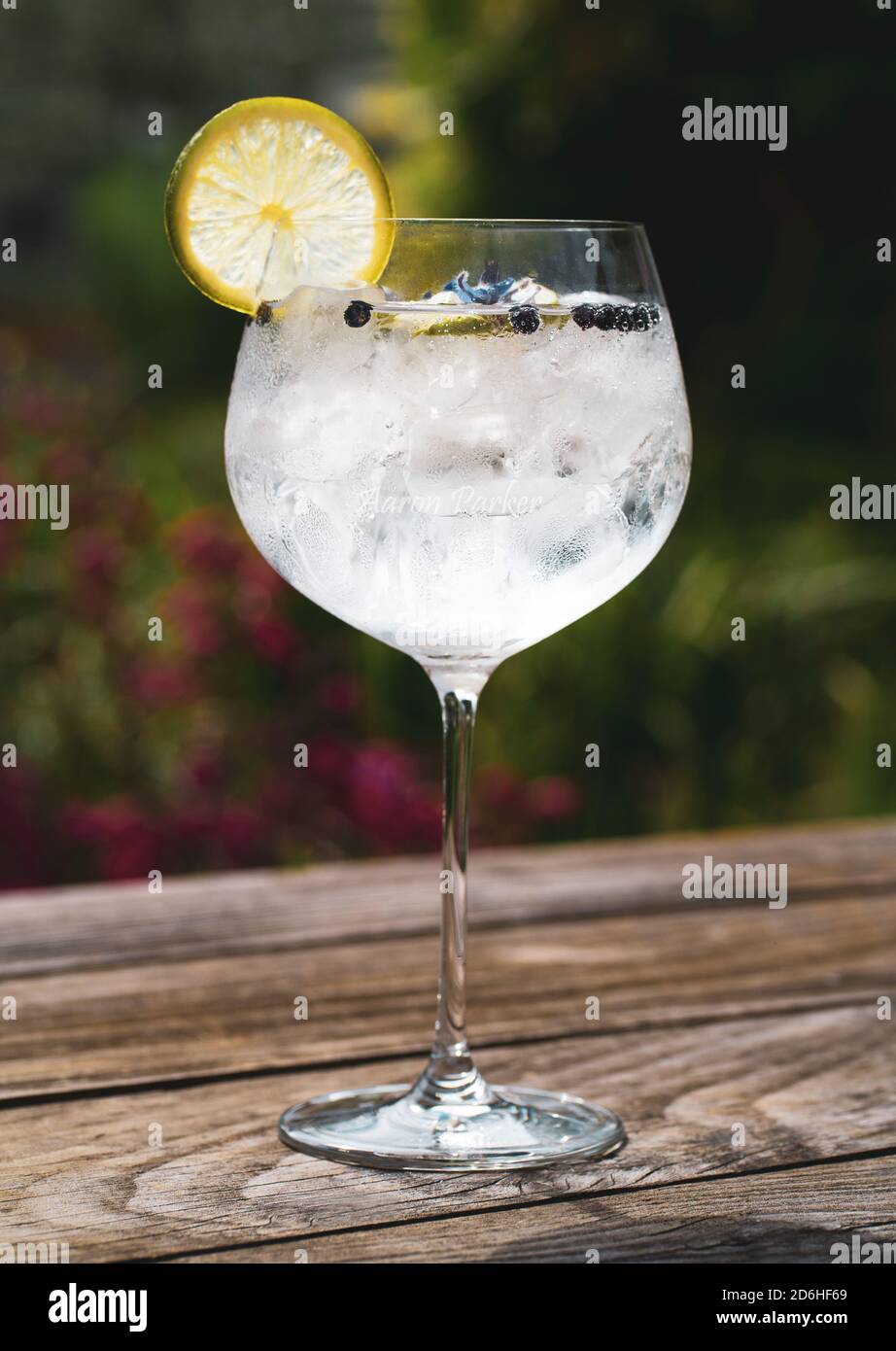 Gin and tonic cocktail drink outside on a wooden table with ice, lemon and lime Stock Photo