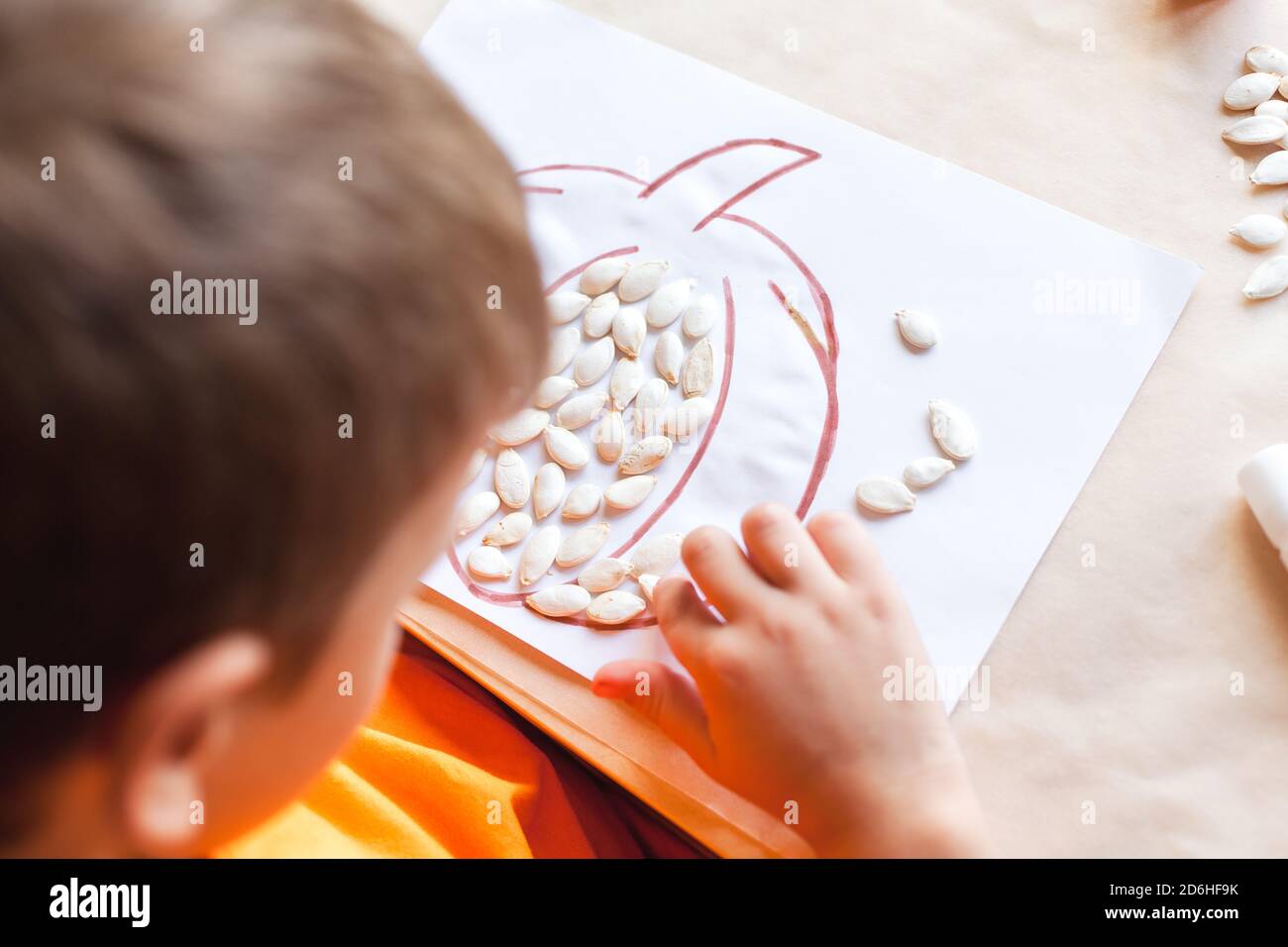 Cute boy making pumpkin from seeds on paper, Halloween DIY concept