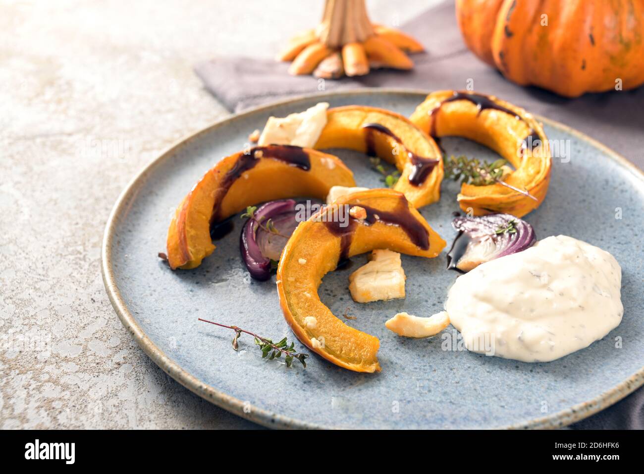 Pumpkin or squash wedges baked with red onions, feta cheese and thyme, also balsamic sauce and a sour cream dip on a gray blue plate, Thanksgiving or Stock Photo
