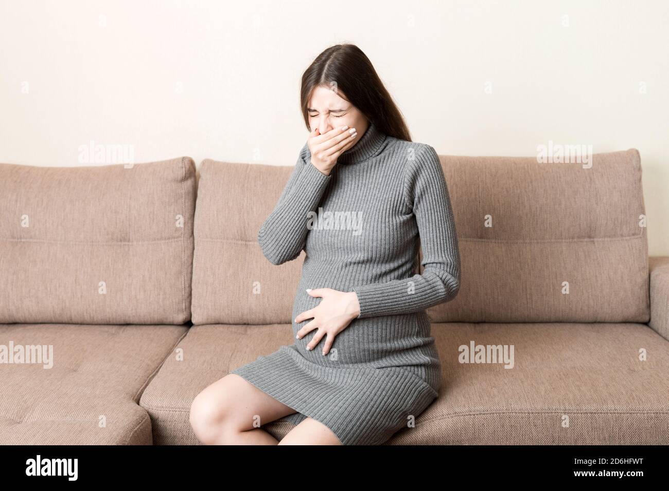 Young vomiting woman sitting on sofa and suffering with nausea