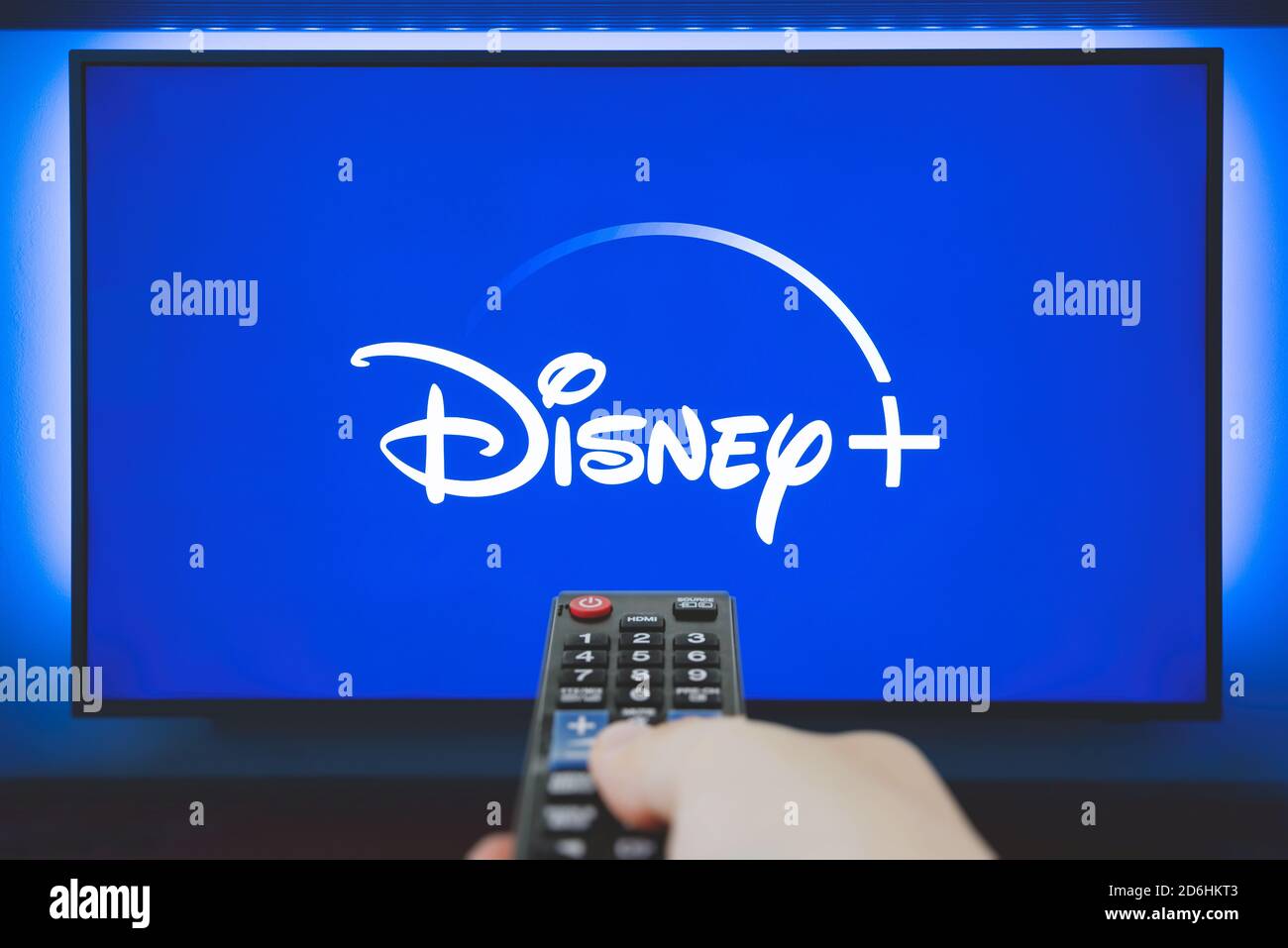 Wroclaw, Poland - OCT 13, 2020: Man holds a remote control. Disney+ logo on TV screen in background. Disney+ is a new online video streaming service Stock Photo