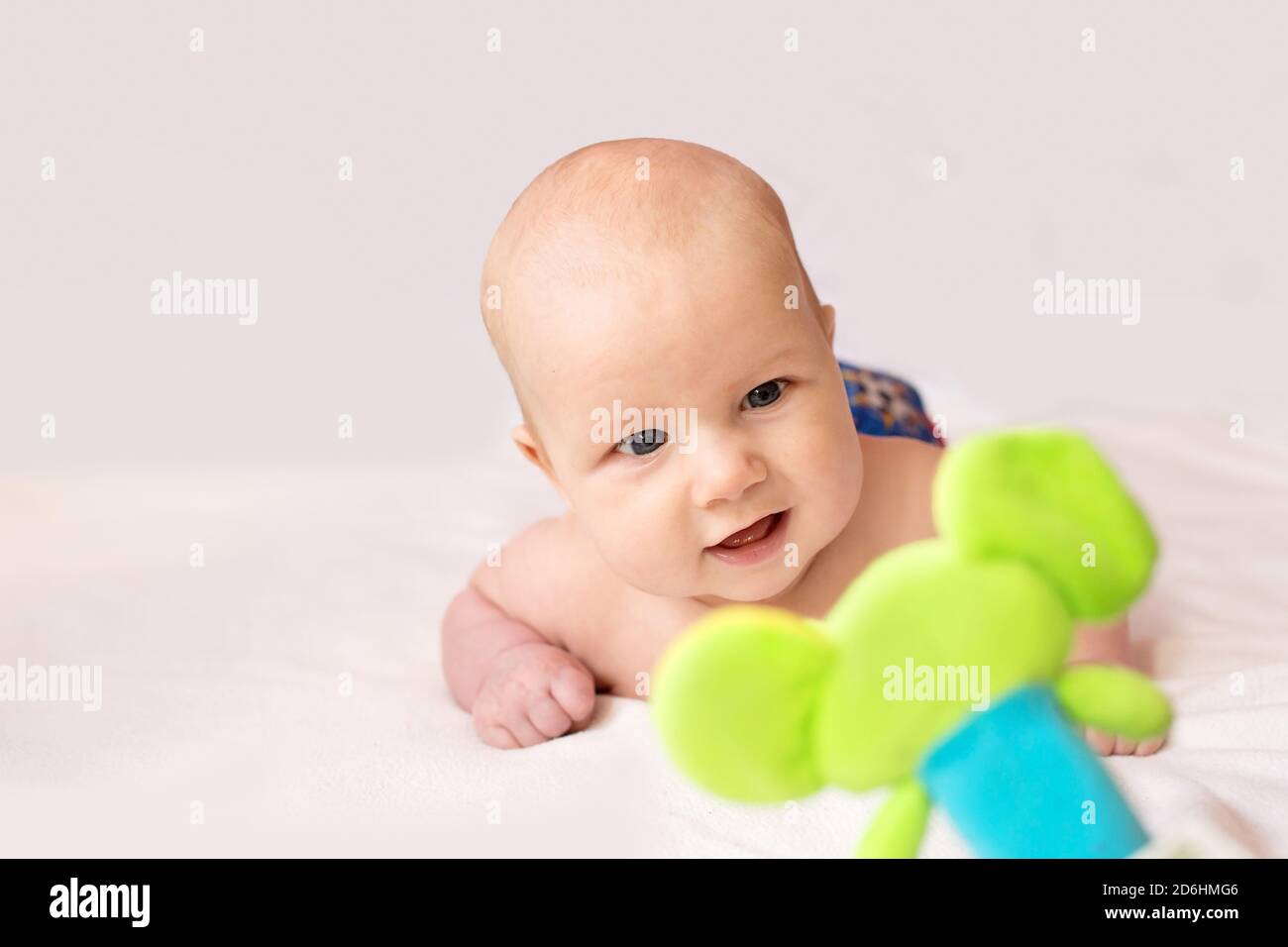 Cute baby lay on stomach, look at colorful toy and smile Stock Photo