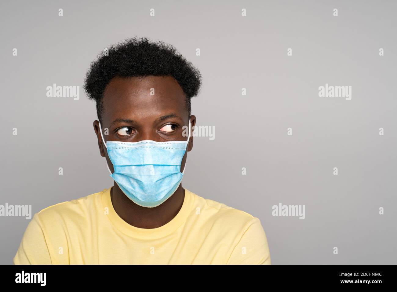 Serious Afro-American man in yellow t-shirt wear face mask looking away at copy space for advertising, offering, product, promotion text, sale, over s Stock Photo