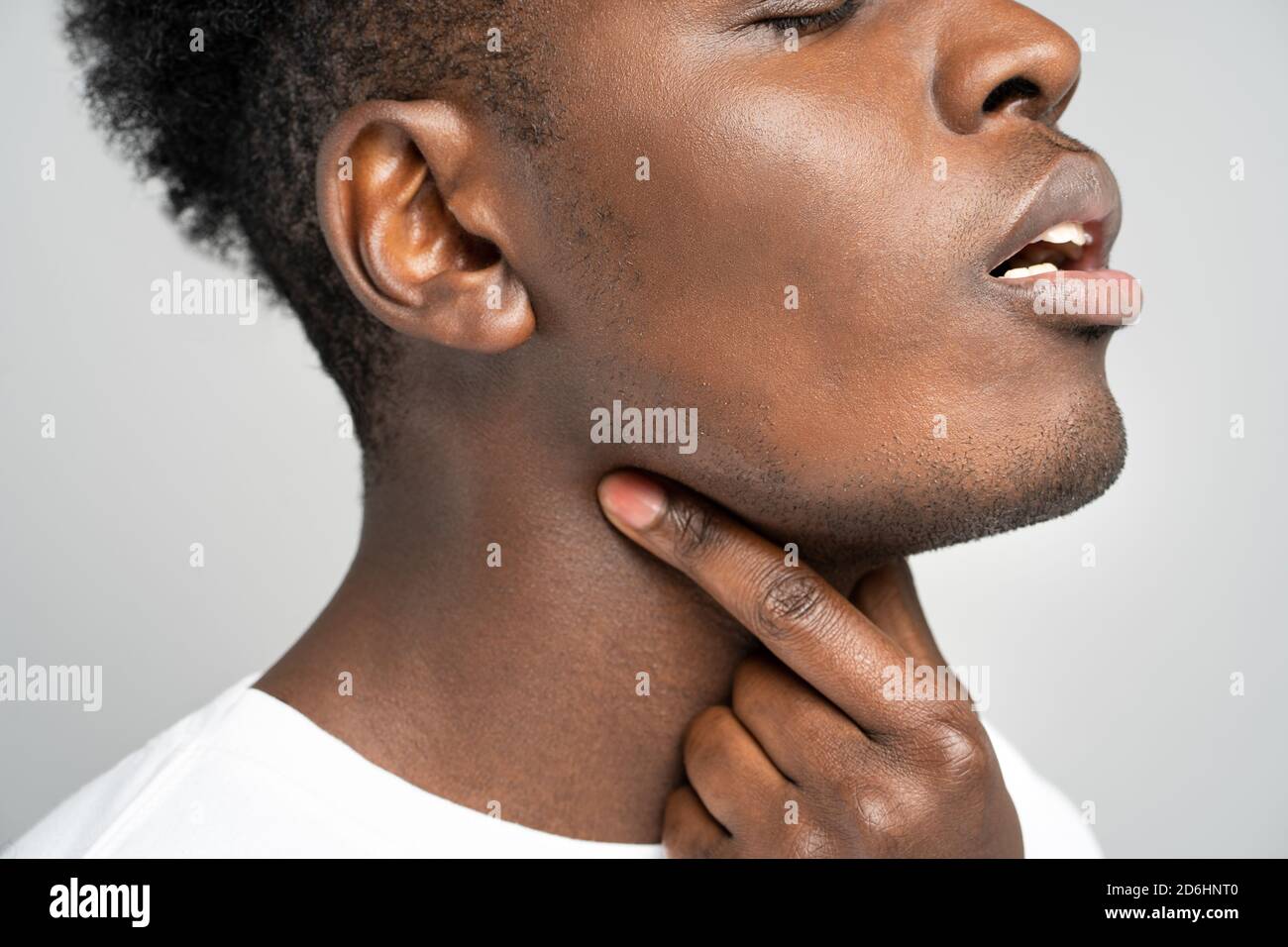 Closeup of afro man touches fingers of sore throat, isolated on gray background. Thyroid gland, painful swallowing, tonsillitis, laryngeal swelling co Stock Photo
