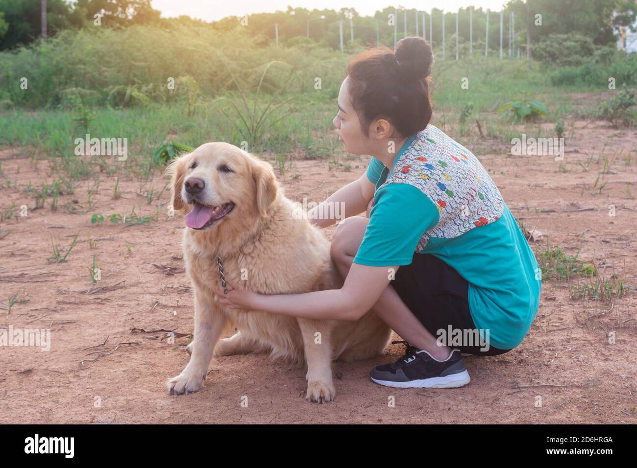 Asian woman playing with her golden retriever dog in a park outdoors ...