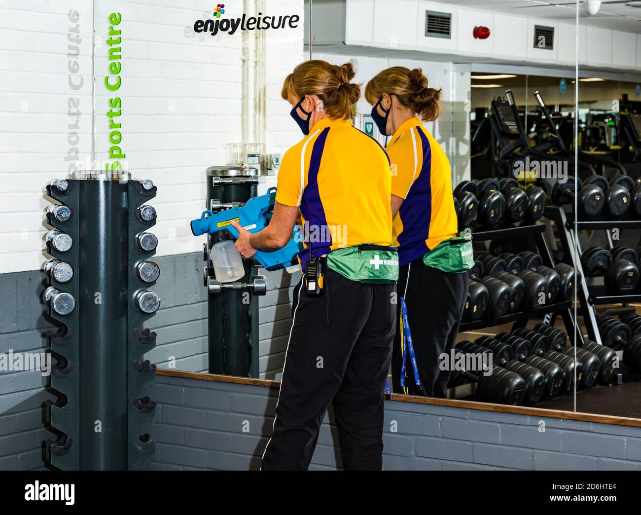 Female staff wearing face mask cleaning gym weights with fogger hygiene sprayer during Covid-19, North Berwick sports centre, East Lothian, Scotland Stock Photo