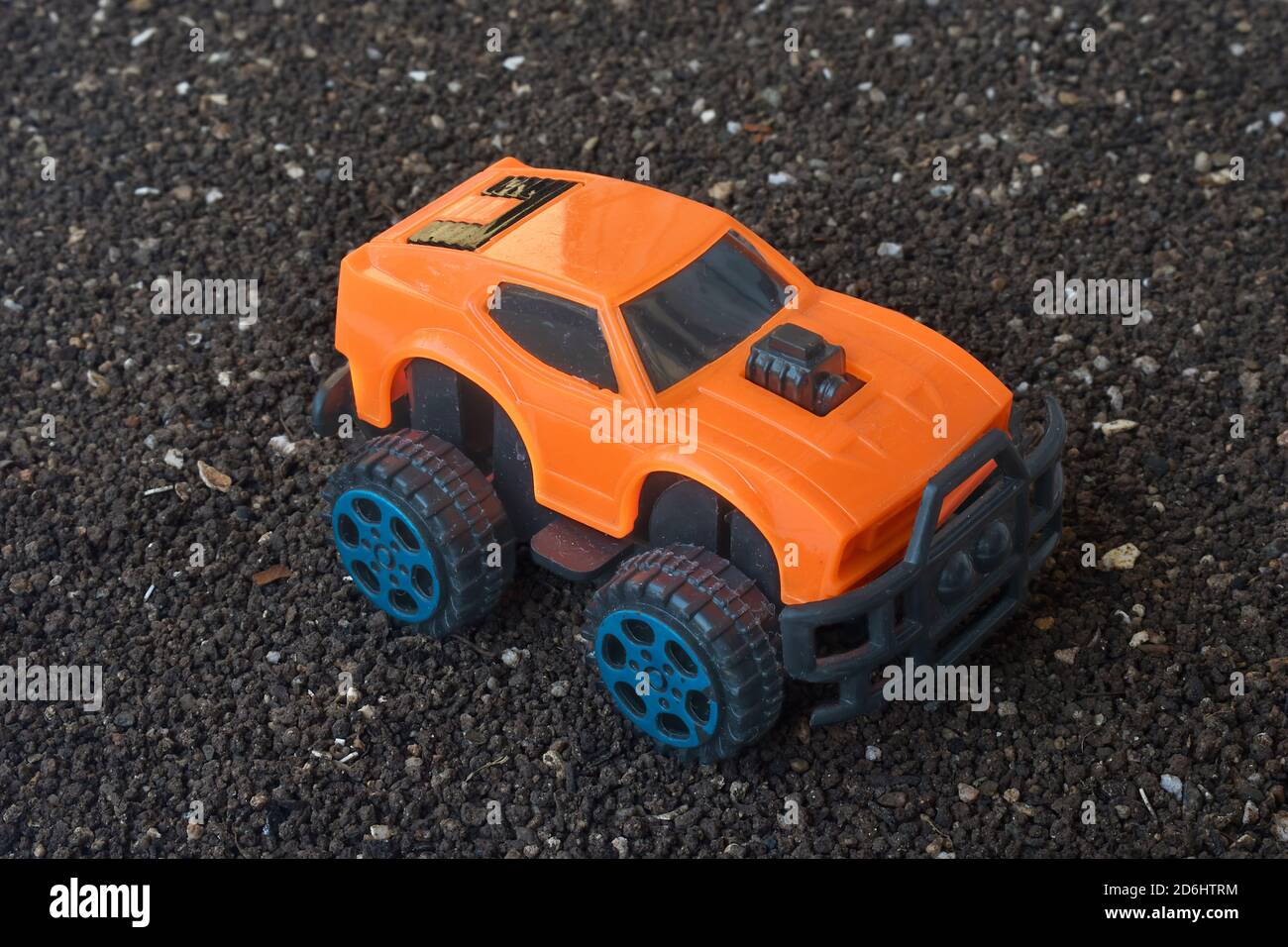 Plastic orange 4x4 car toy on dirt ground,  mini suv vehicle. Stock Photo
