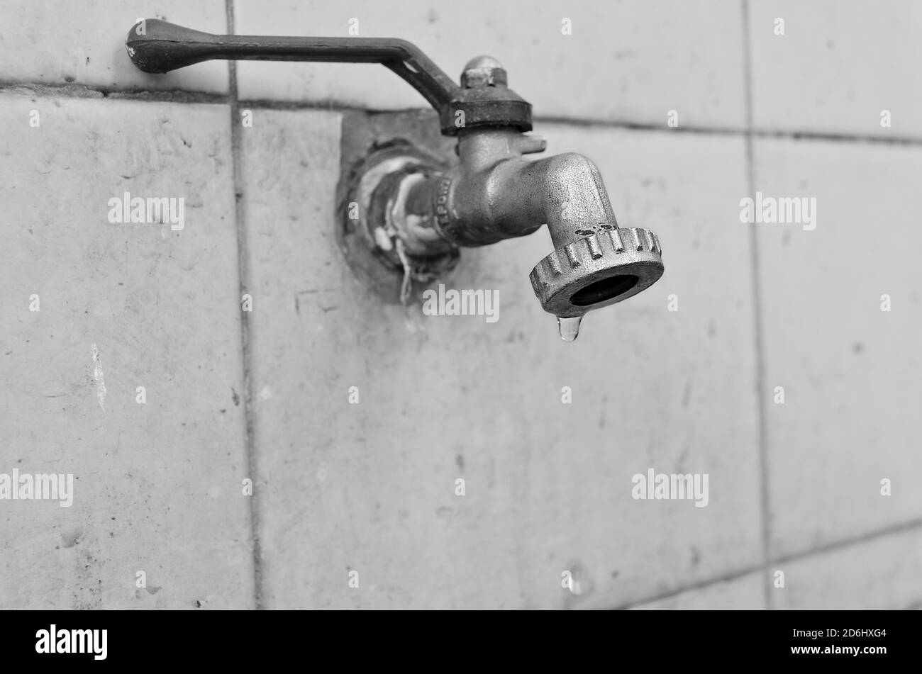 Closeup of waterdrops falling from a grunge faucet placed on white tiles Stock Photo