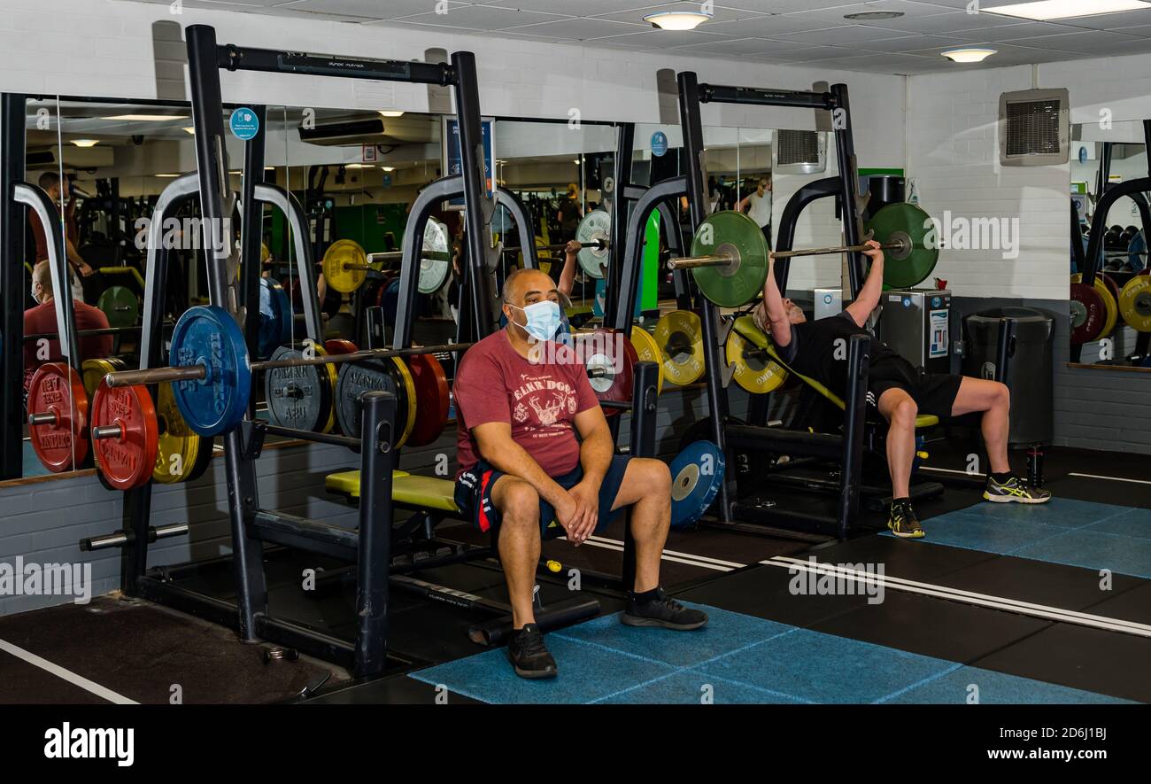 Man wearing face mask lifting weights in gym during Covid-19 pandemic after lockdown easing, North Berwick sports centre, East Lothian, Scotland, UK Stock Photo