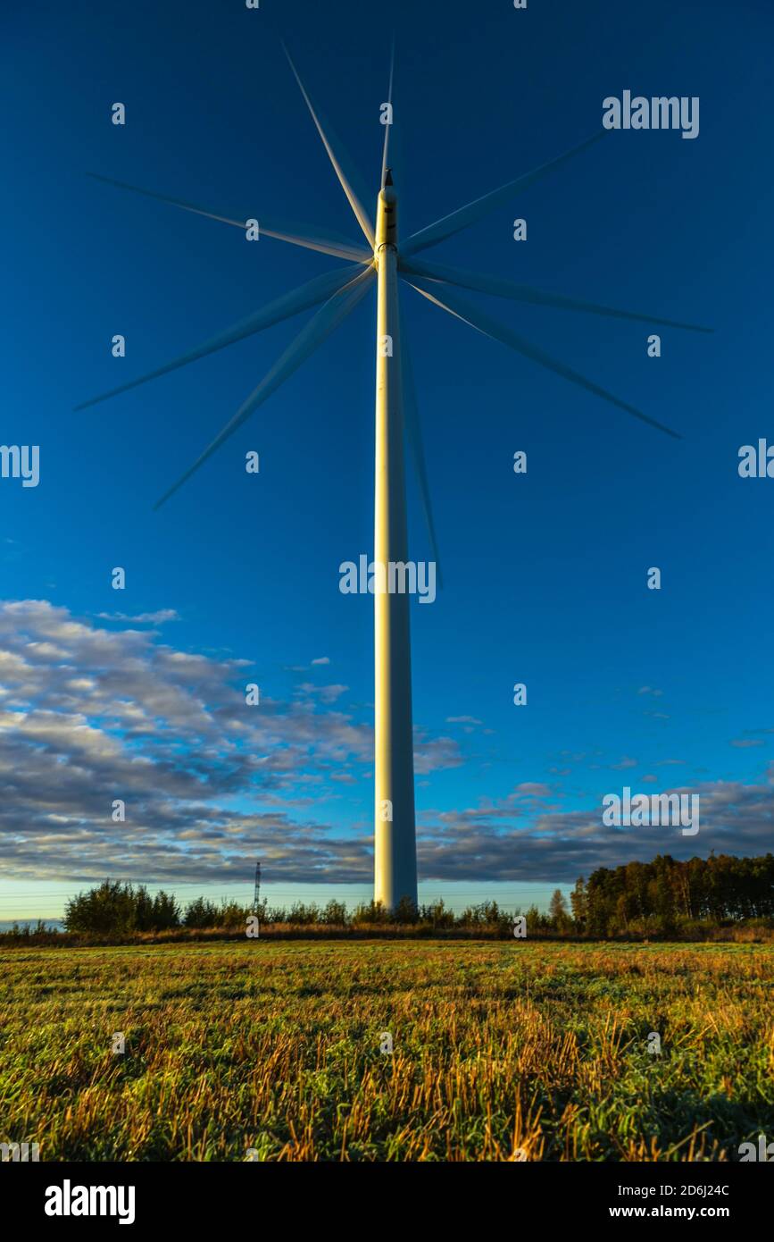 wind generator in white rotates on a background of blue sky with clouds and green grass on the ground Stock Photo