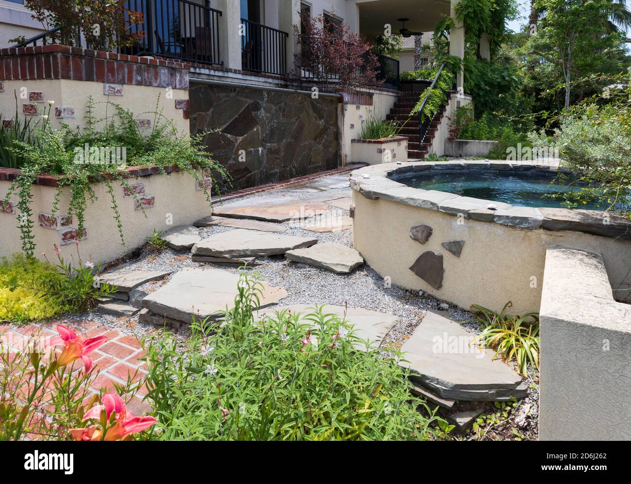 A South Carolina garden in May. A raised hot tub, waterfall, and planters frame a flagstone patio with gravel. Stock Photo