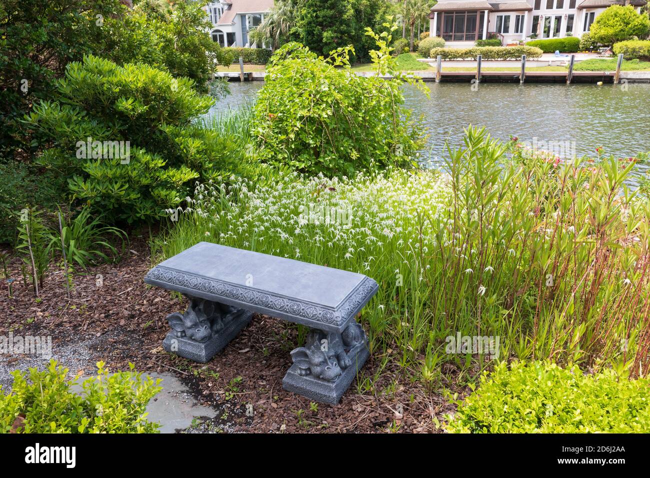 A South Carolina garden in May. White star grass in front of a stone bench beside a canal. Stock Photo