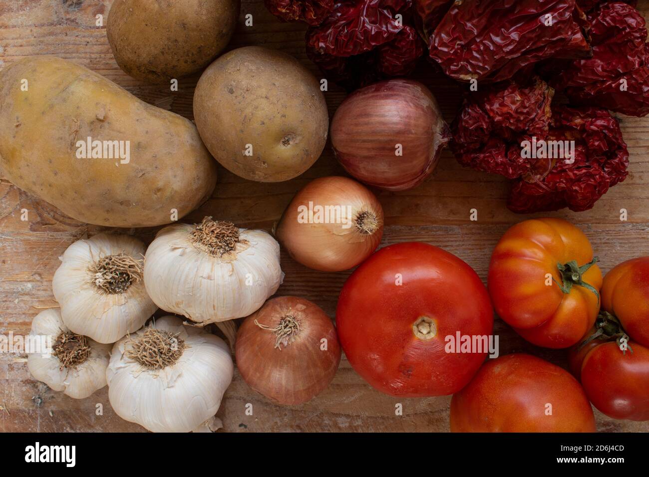 Food ingredients on traditional wooden background. Tomatoes, potatoes, onions, garlic and dried peppers. Stock Photo