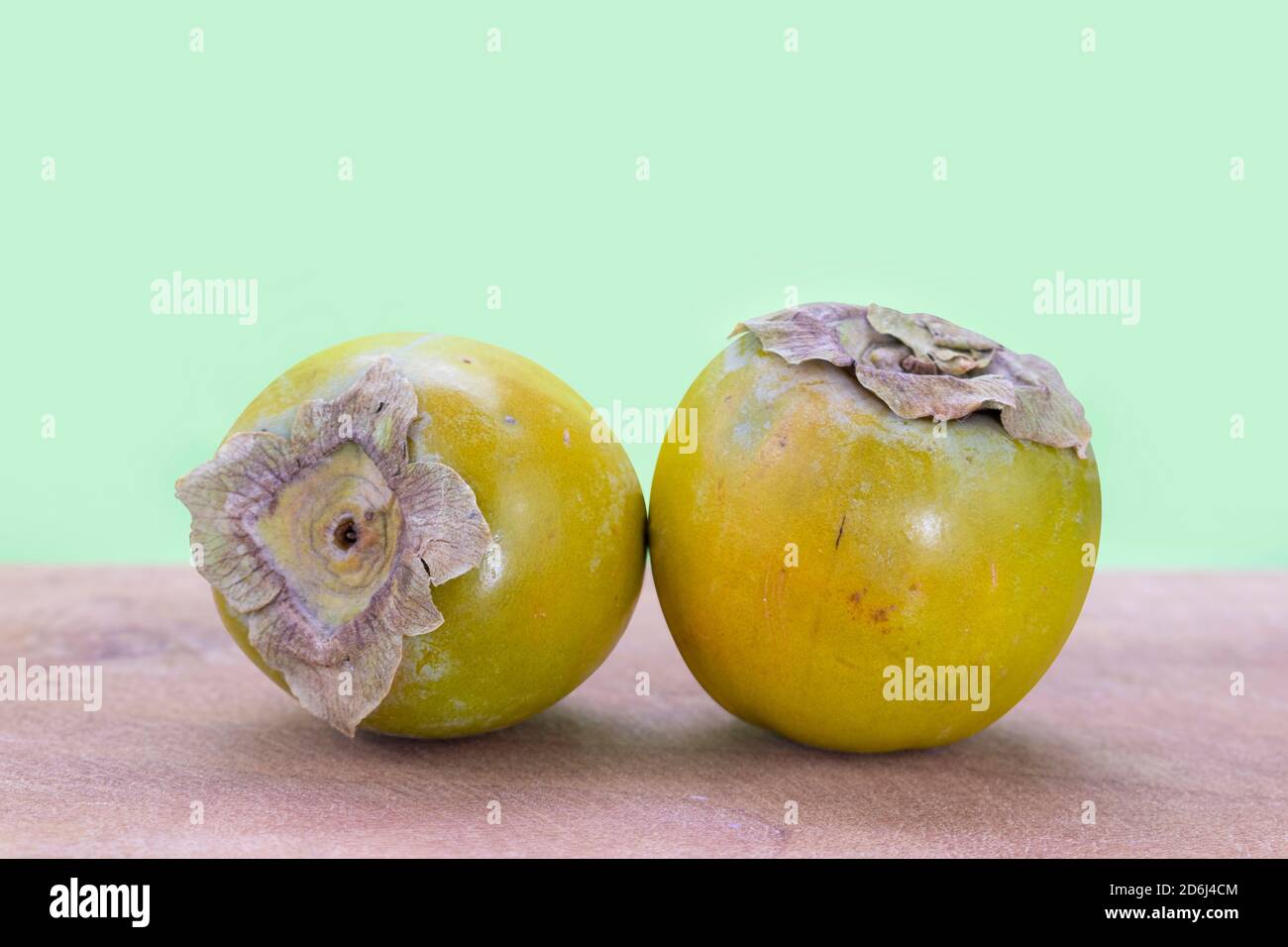 Fresh unripe fuyu persimmons on wood and green background Stock Photo