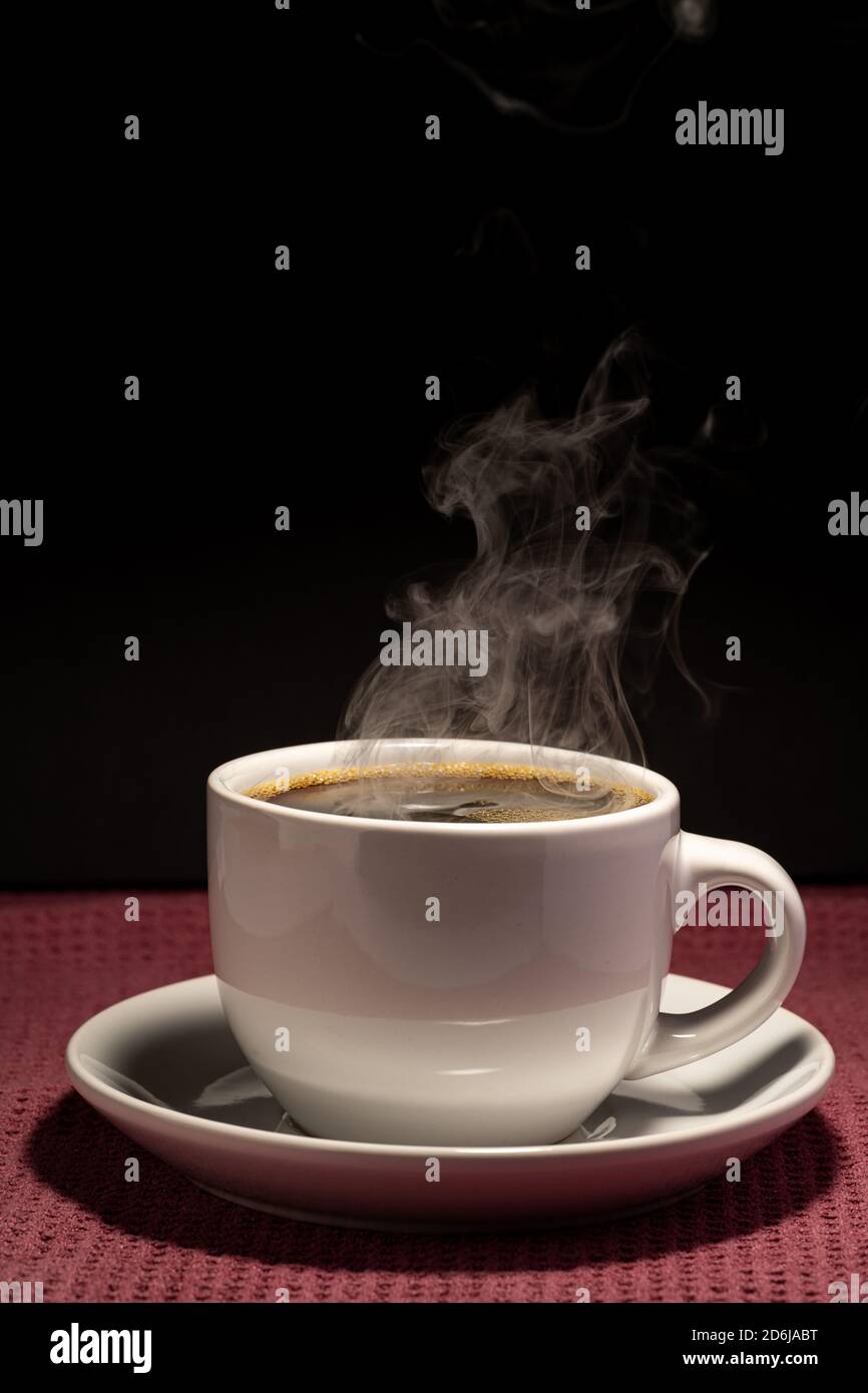 Coffee steaming in a cup with saucer isolated on a black background on ...