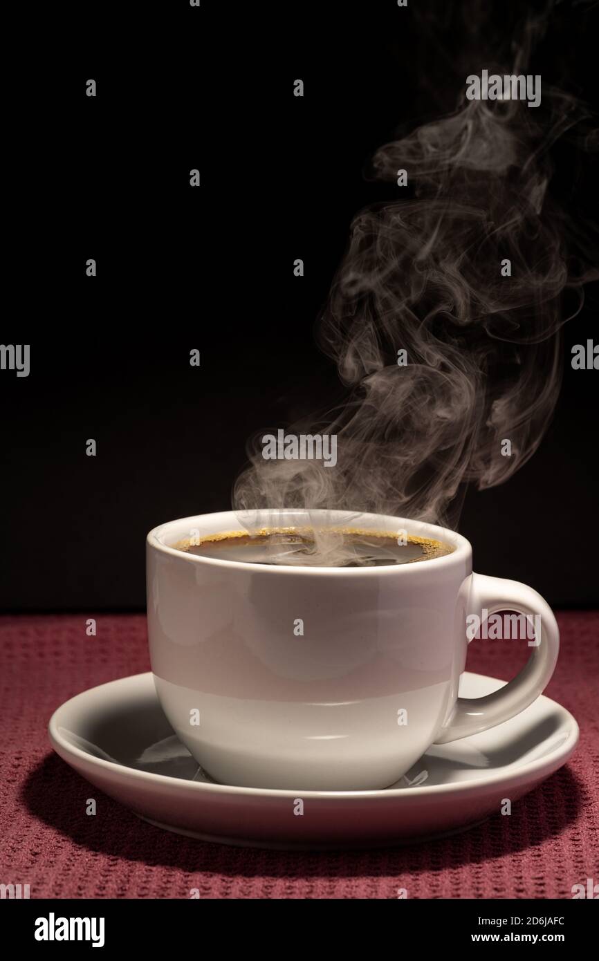 Coffee steaming in a cup with saucer isolated on a black background on ...
