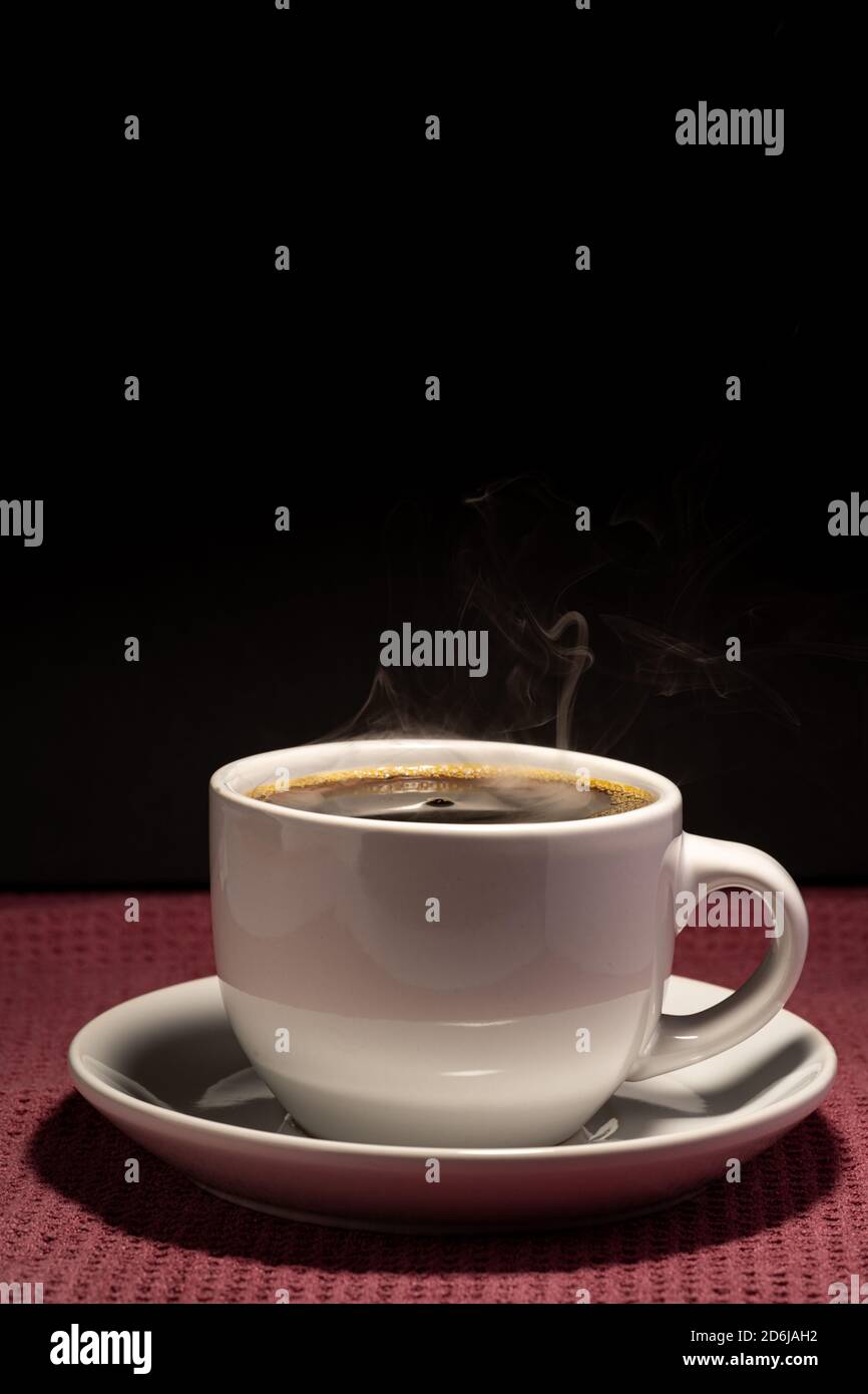 Coffee steaming in a cup with saucer isolated on a black background on ...