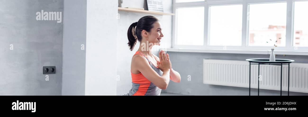 Panoramic shot of sportswoman with praying hands near coffee table at home Stock Photo