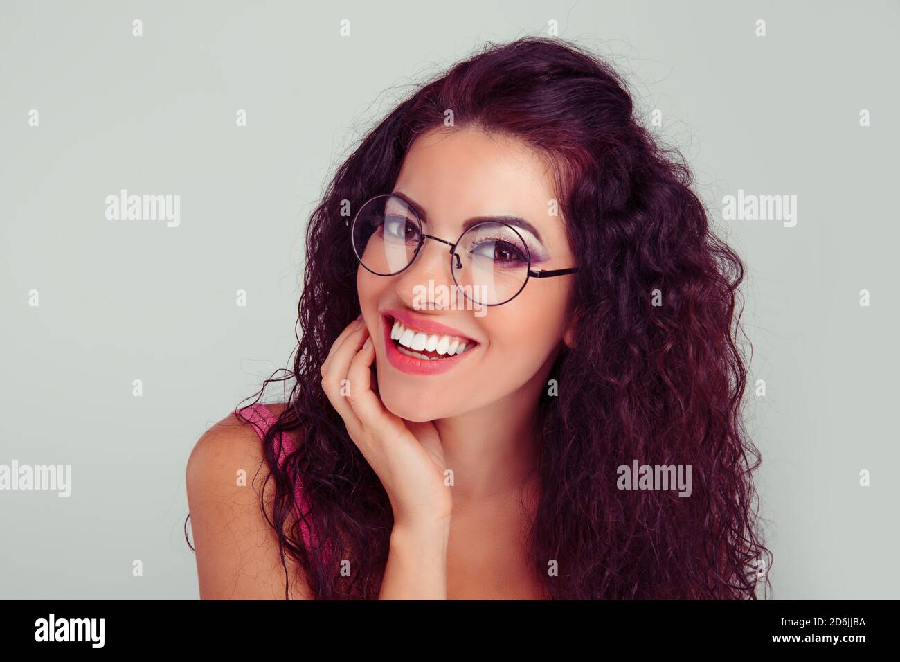 Closeup portrait young hispanic latina woman wearing big round spectacles with thin black frame, touching temples with fingers, smiling with expressio Stock Photo