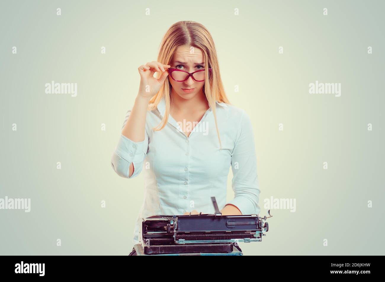 Skeptical woman at typewriter looking at you camera doubtfully isolated on light green yellow background with copy space. Writer having doubts. Skepti Stock Photo