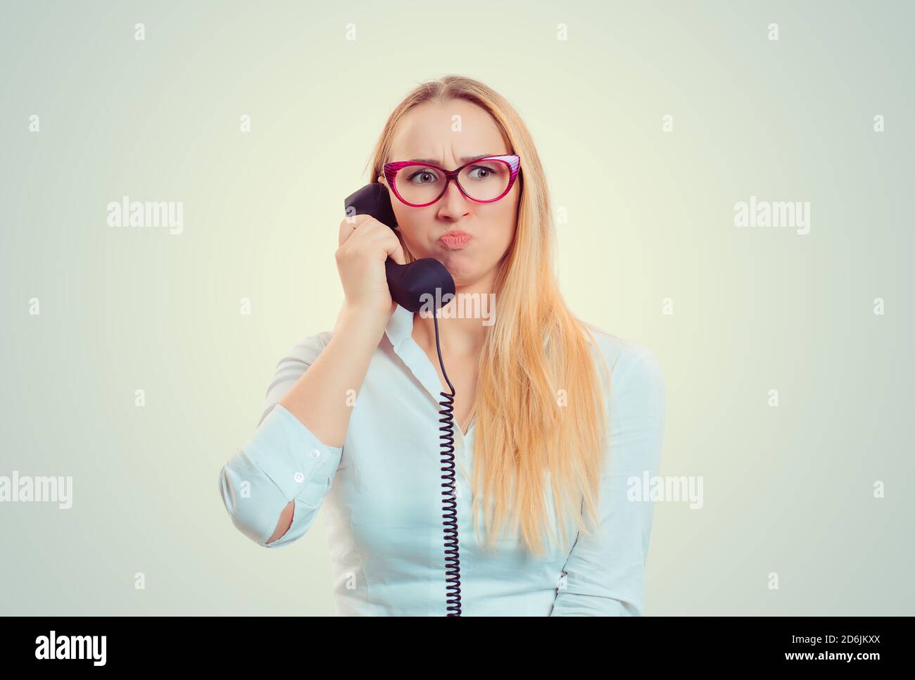 Misunderstanding and distant call. Upset young woman talking on phone frustrated by the call isolated on light green yellow background. Girl hears fru Stock Photo