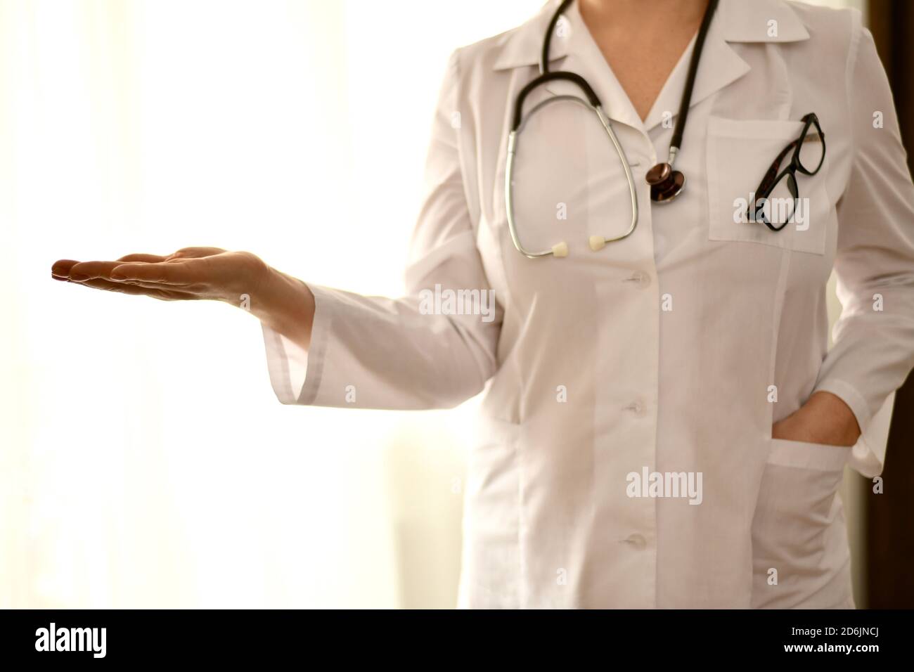 The doctor stands in front, one empty hand palm outstretched, the other hand in the pocket of a white robe.  Stock Photo