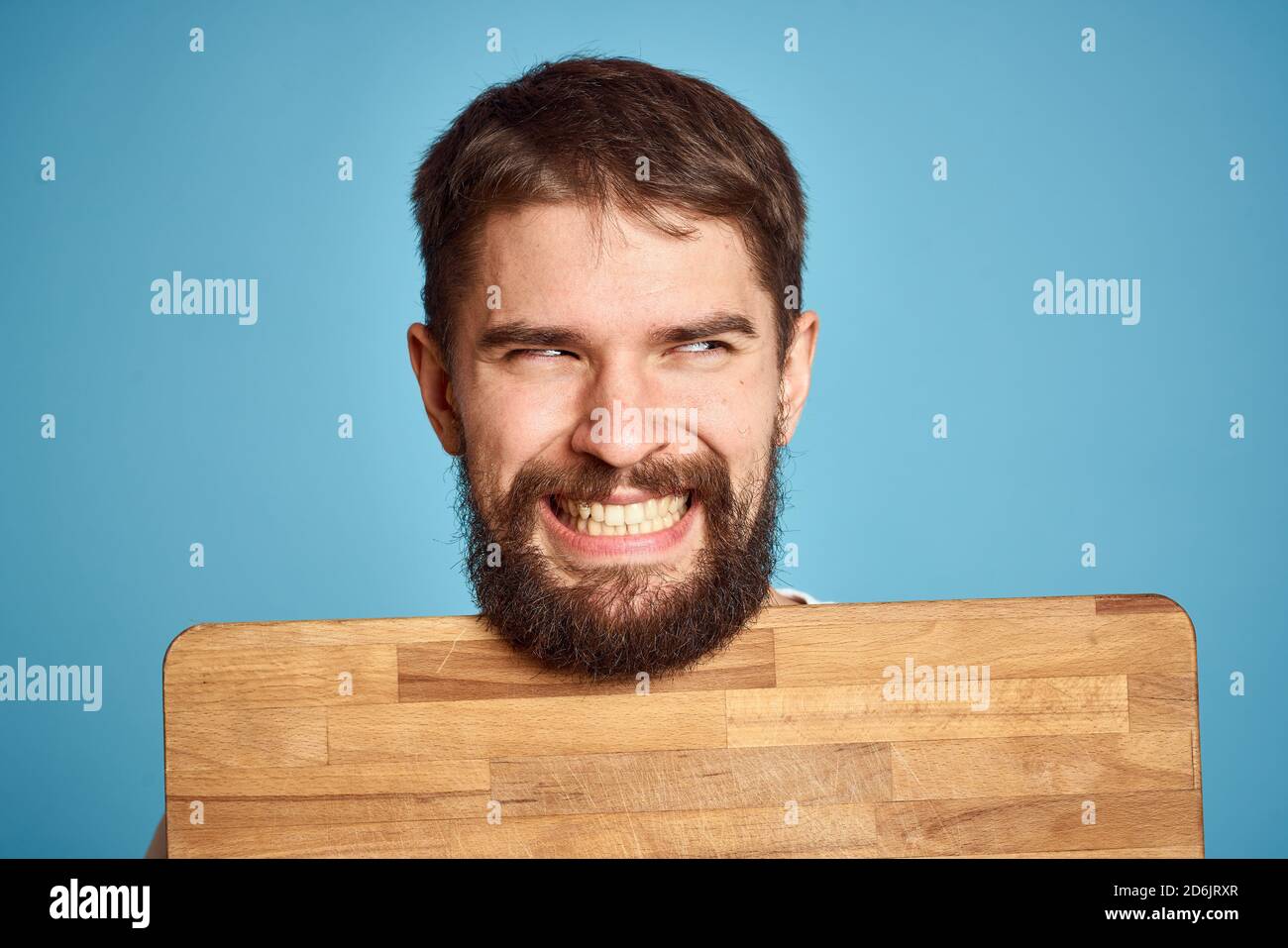 cute man with kitchen board near face on blue background emotions smile