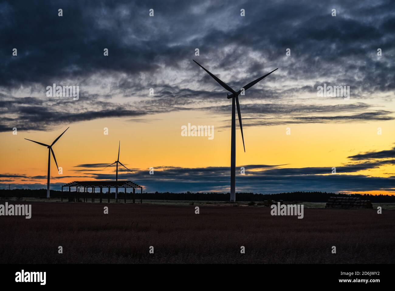 wind generators, hay rollers and a skeleton of a building in a meadow with wind generators rotating and generating electricity near the forest and clo Stock Photo