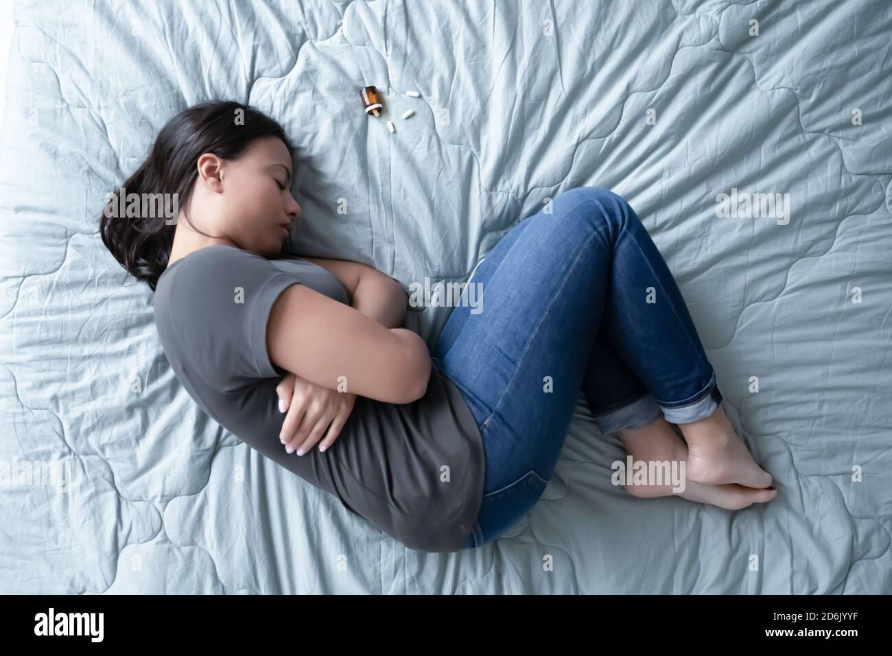 Top view of depressed woman lying on bed with pills Stock Photo