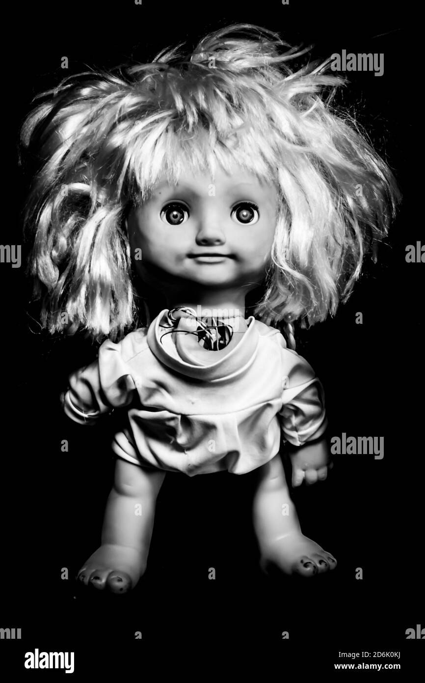 Creepy girl doll face. It seems like character of horror movie. Angry baby doll, fear of living ghost. Halloween concept. Black and white shot, low-ke Stock Photo